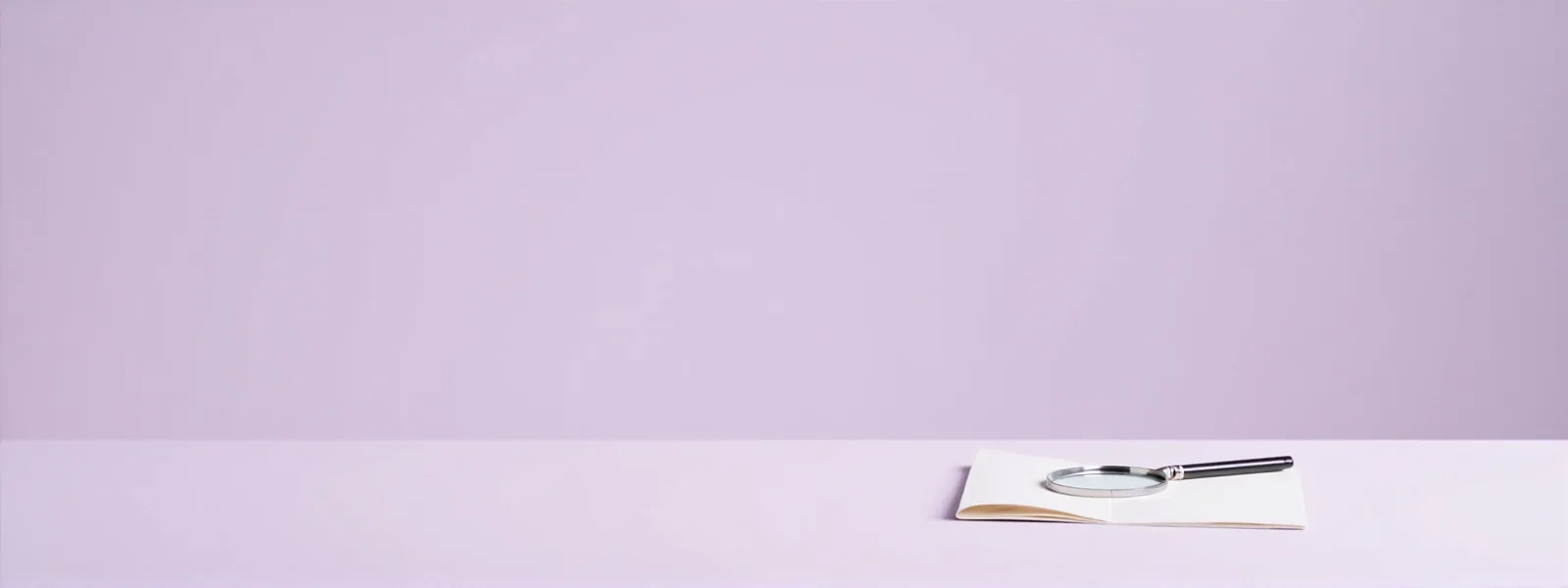Wide editorial banner of a softly lit editor desk with a magnifying glass on a notepad